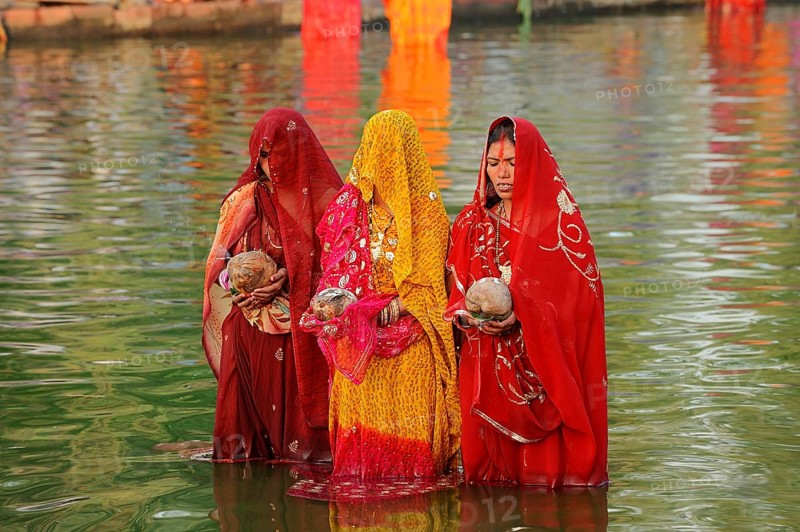 Women wearing saris with offerings standing in water during the Hindu Chhath Festival