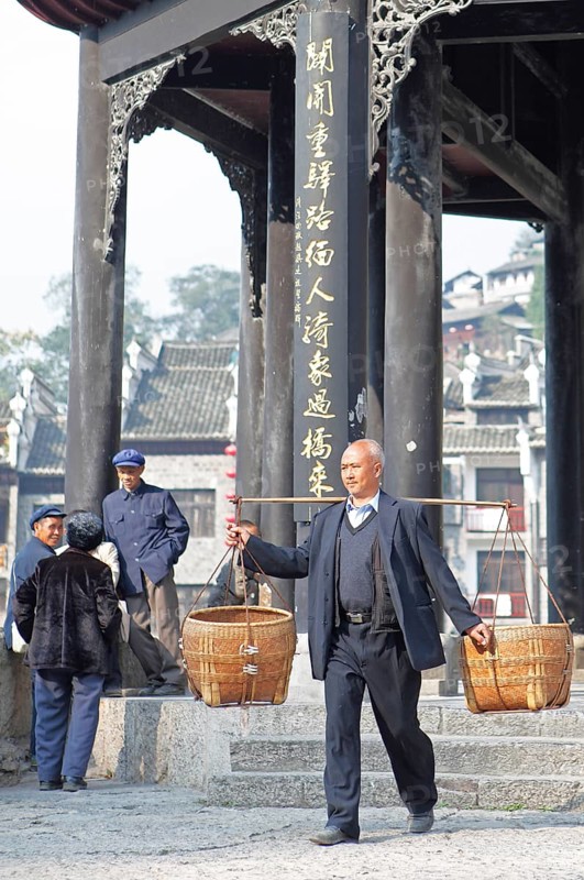 Man shouldering bamboo baskets in front of the Kuixingge Pagoda