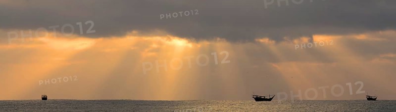 Sun beams above the Arabian Sea with the silhouettes of typical dhows