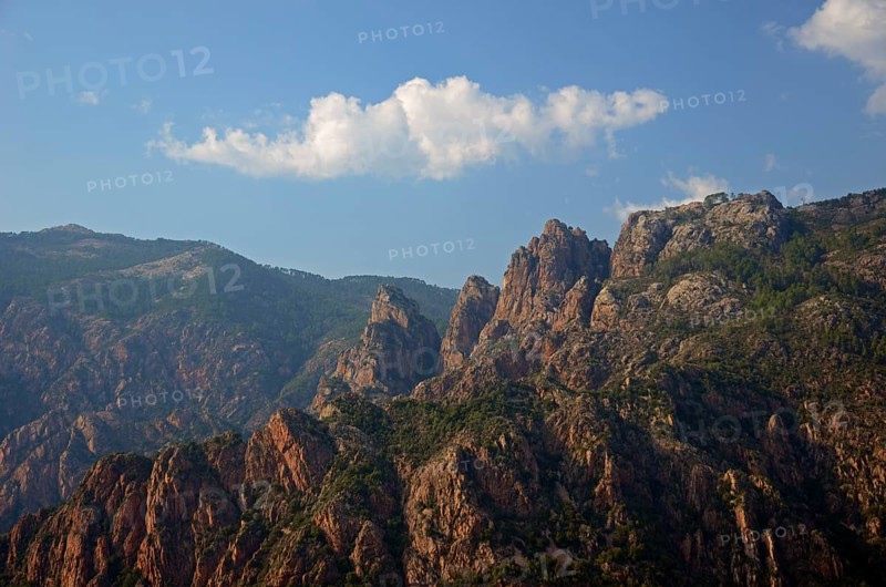 The typical rocky mountains of western Corsica near Evisa below a blue sky with a lone white cloud. Evisa illuminated by warm evening light surrounded by mountains. Evisa is in the department Corse-du-Sud