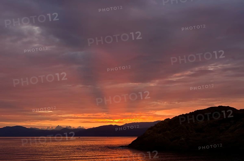 The rising sun forms sun beams behind the rocks of the island Ile de la Pietra near L'Ile-Rousse. L'Ile-Rousse is in the department Haute-Corse