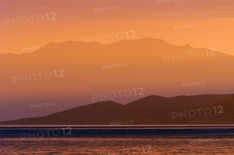 The rising sun forms sun beams behind the rocks of the island Ile de la Pietra near L'Ile-Rousse. L'Ile-Rousse is in the department Haute-Corse
