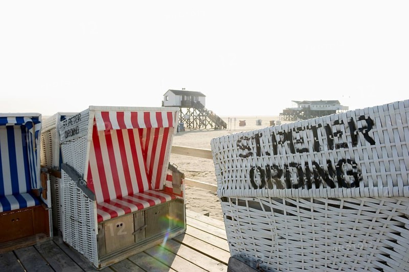 Roofed wicker beach chairs on the beach in front of houses on stilts
