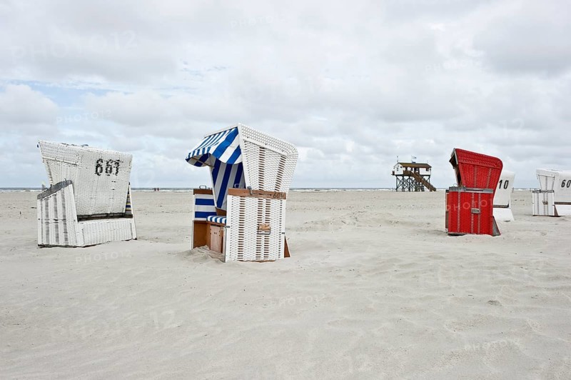 Roofed wicker beach chairs on the beach in front of a house on stilts