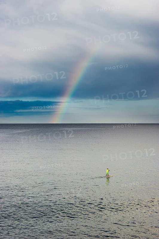 Stand up paddler with rainbow over the sea