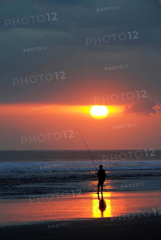 Fisherman fishing at sunset on the beach