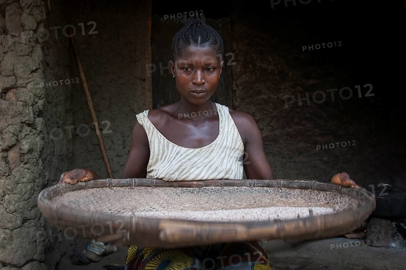 Woman separating grain from the chaff outside a hut