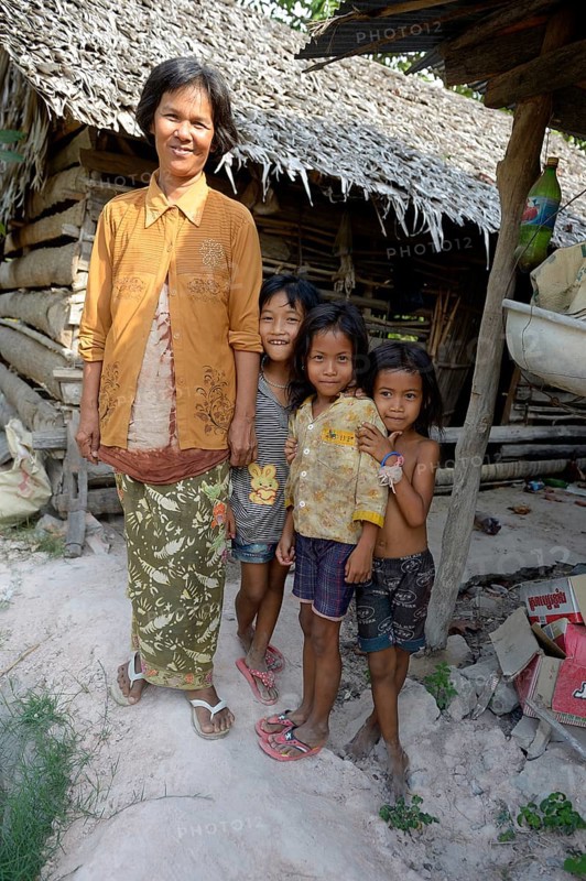 Woman standing with three girls in front of a hut made of wood and straw