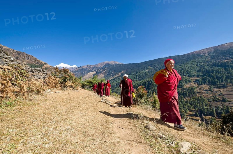 Monks and nuns wearing red cloths walking on a small path along a mountain slope