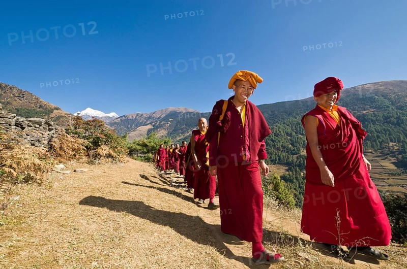 Monks and nuns wearing red cloths walking on a small path along a mountain slope