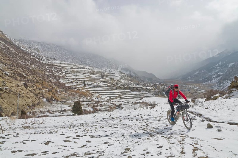 Cyclist riding his bike in the snow up towards Thorong La Pass (5416 m)
