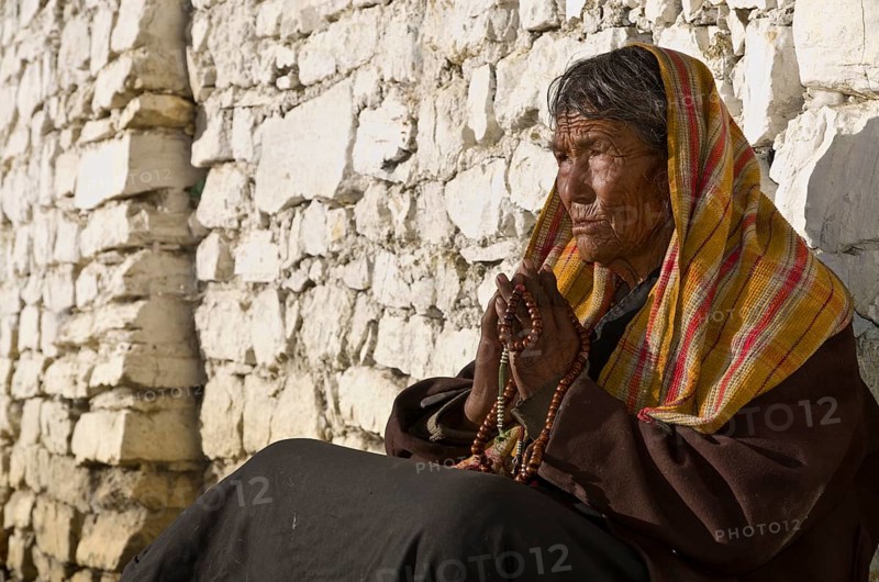 Old local woman praying in front of a brick wall