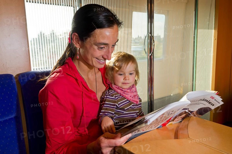 Young mother with child reading in a booklet inside ICE train