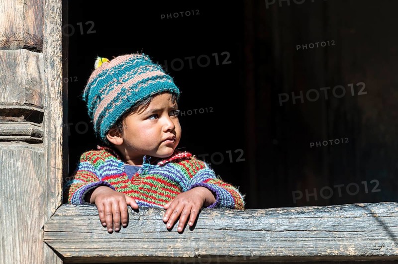 A small child looking out of the window of a wooden house