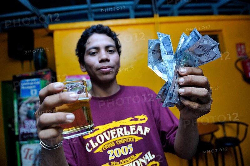 Young man in a brothel holding a beer and condoms in his hand
