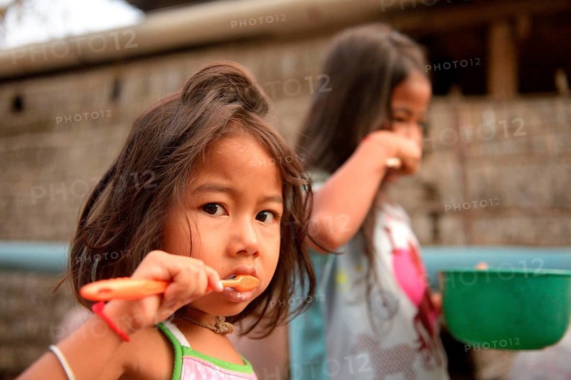 Two girls brushing their teeth outside a house