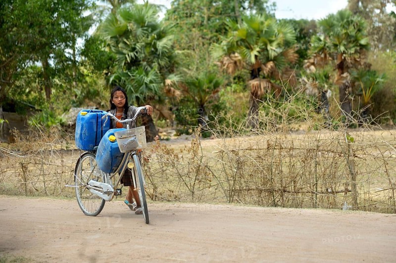 Girl transporting two canisters with water from the reservoir of the nearby pagoda on her bike to her home