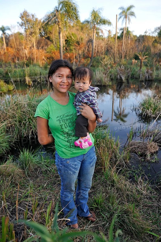 Young mother holding a child in her arms in front of a pond in the community of Mbya-Guarani Indians