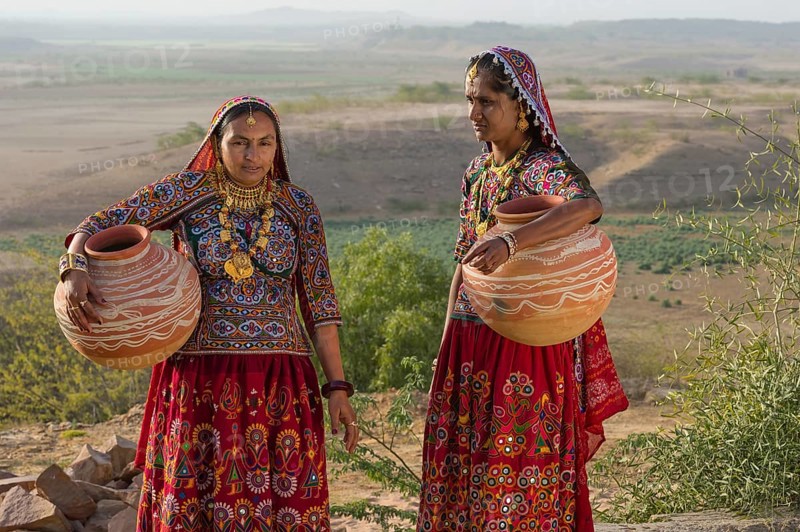 Two Ahir Women in traditional colorful clothes carrying water in a clay jug
