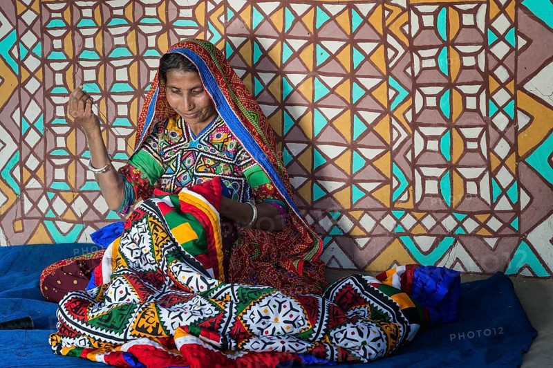 Woman in traditional clothes sewing handicraft in front of a house