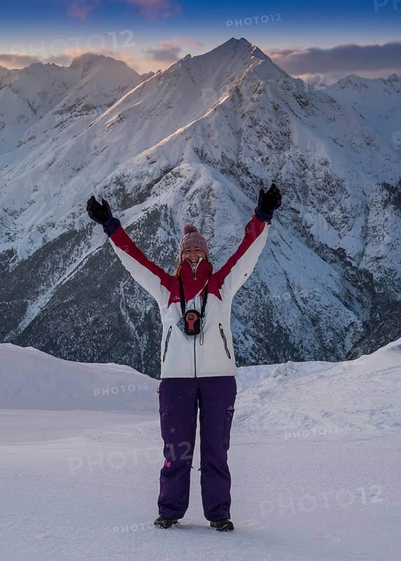 Woman with arms outstretched standing in front of an Alpine panorama
