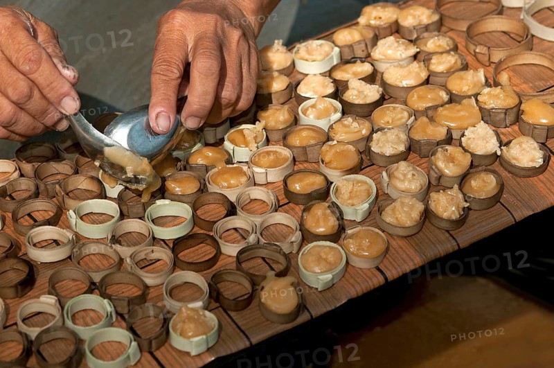 Caramelized palm sugar being filled into small moulds made of strips of palm leaves for the production of traditional palm sugar candies