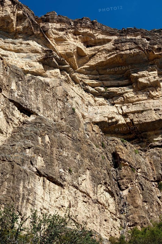 Rock face at the western flank of the Grand Canyon of Oman in the Wadi at Nakhar with hikers on the fixed climbing route leading to the exit from the gorge