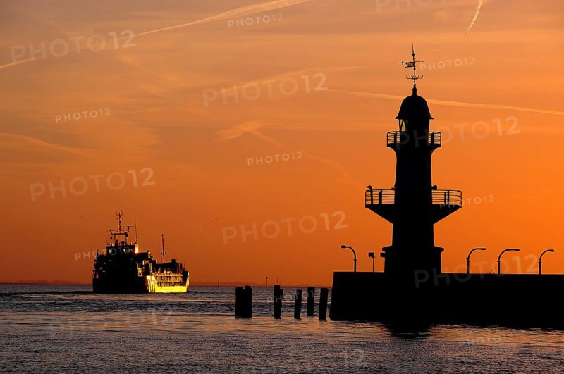 Cargo ship and silhouette of the Brunsbuttel Mole 1 lighthouse in front of a evening sky