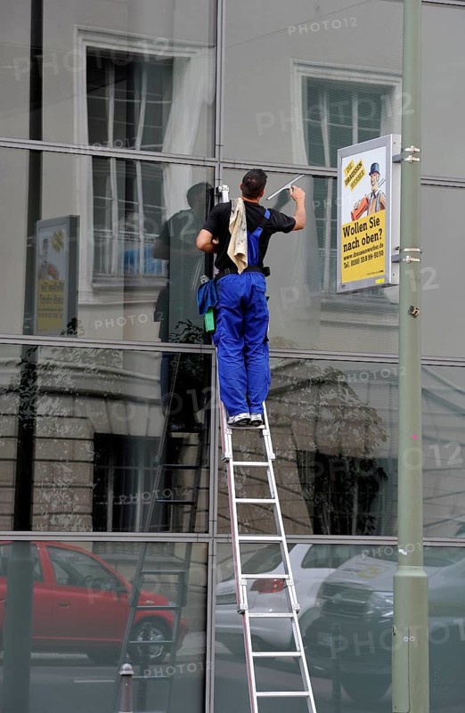 Window cleaner standing on a ladder cleaning a glass facade