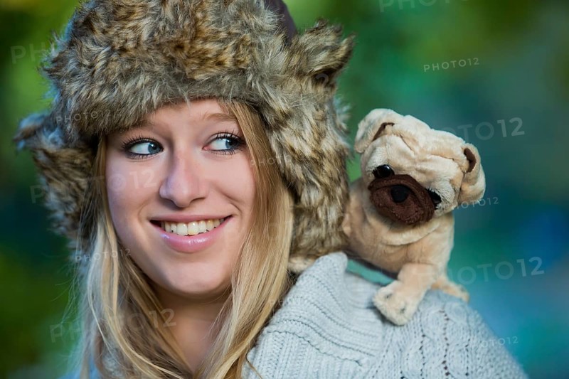 Young woman wearing a fur hat with a plush pug on her shoulder