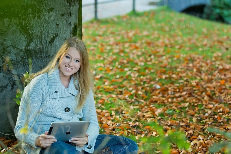 Young woman leaning against a tree in the park with a tablet PC
