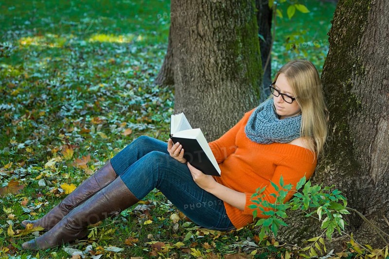 Young woman wearing glasses sitting in the park and reading a book