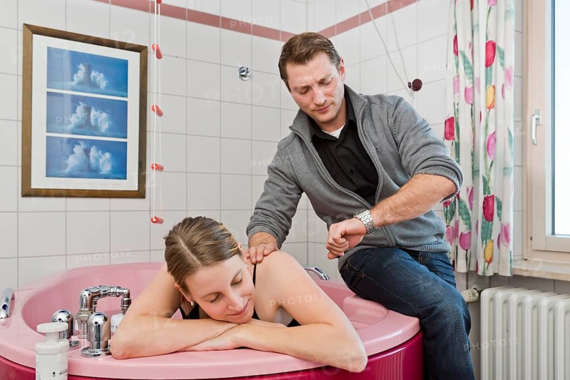 Expectant father looking annoyed at his watch while his wife is resting in a break between contractions