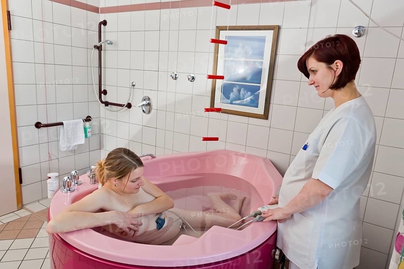 Woman during childbirth with a cardiotocography or CTG in a birthing bath in the maternity delivery room with her midwife