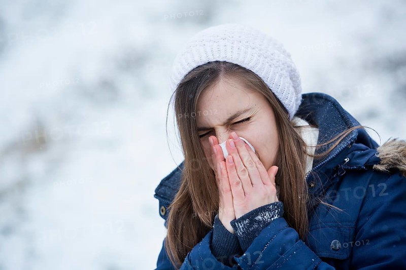Young woman wearing winter clothes blowing her nose