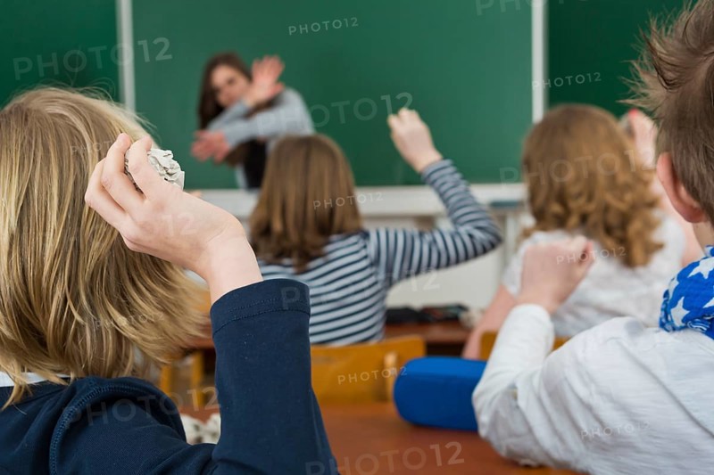 School children in a classroom throwing paper balls at the teacher