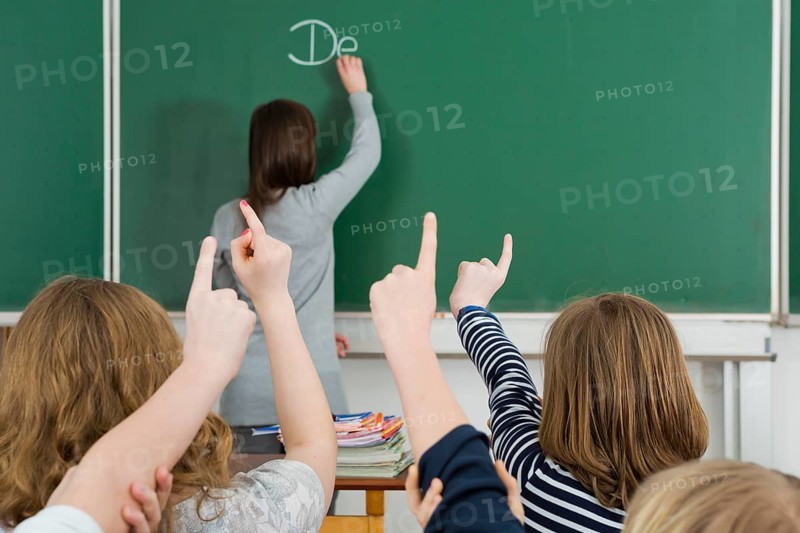 School children raising their arms to answer during class