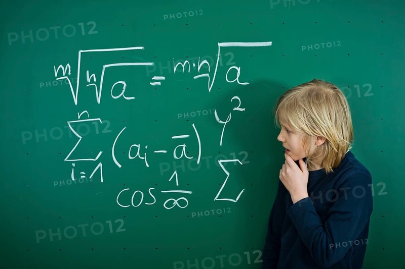Schoolboy pondering a mathematical formula on a school blackboard