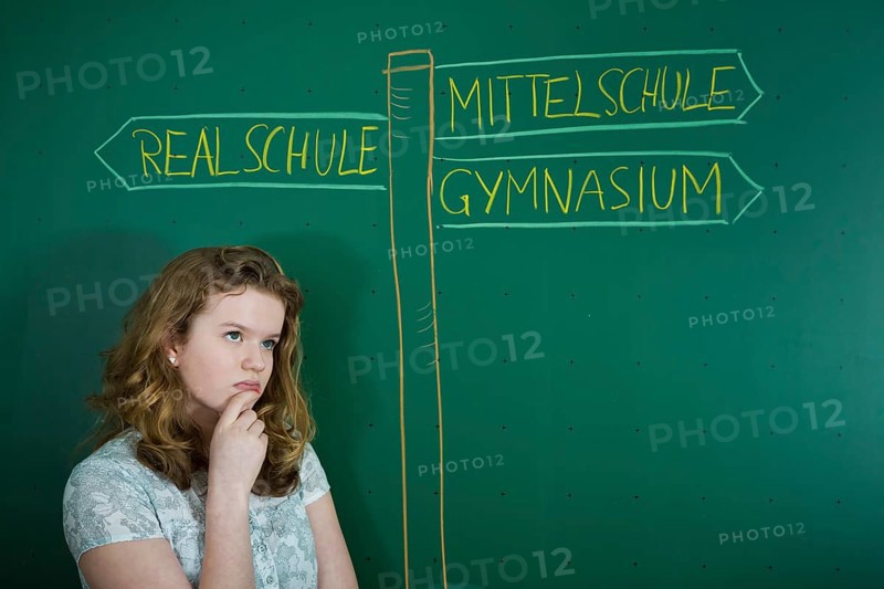 Girl pondering in front of school signs drawn on a blackboard with the signpost directing to the varying types of German secondary schools