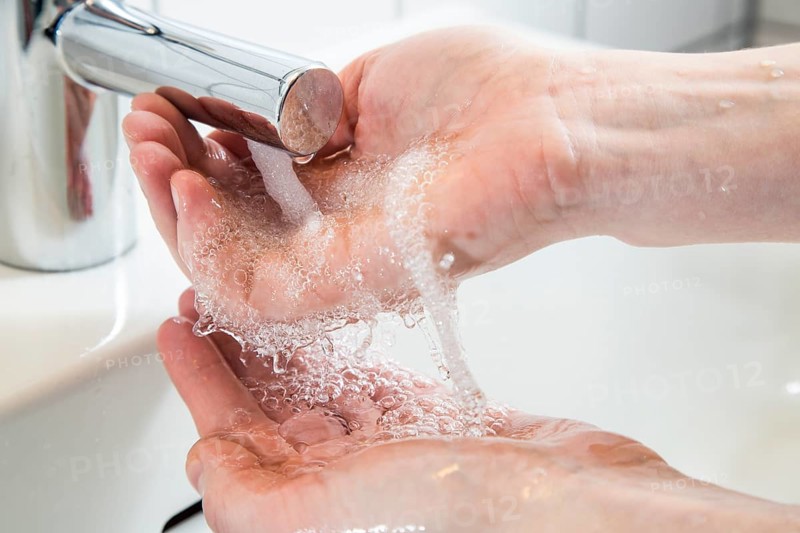 Person washing their hands under running water from a faucet
