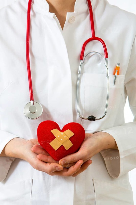 Female doctor holding a red heart with a plaster in her hands