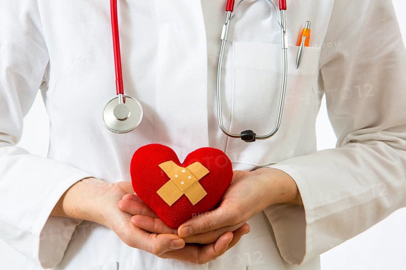 Female doctor holding a red heart with a plaster in her hands
