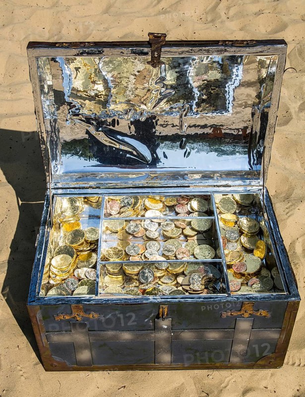 Treasure chest with gold and silver coins on the sand