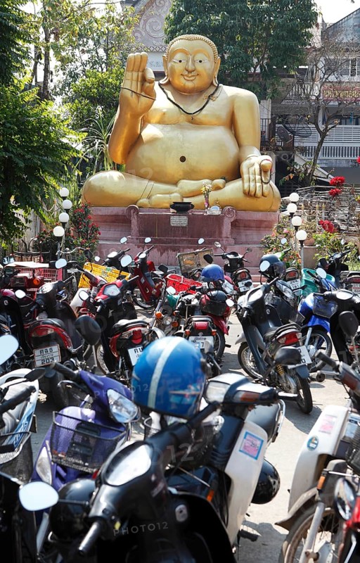 Parking lot for motor scooters in front of a large golden Buddha statue