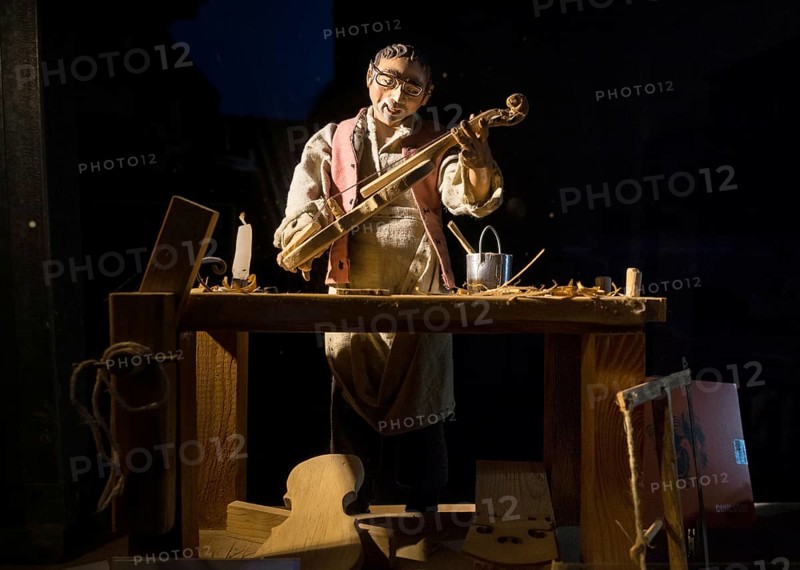 Violin maker as wooden figure at work in violin making workshop