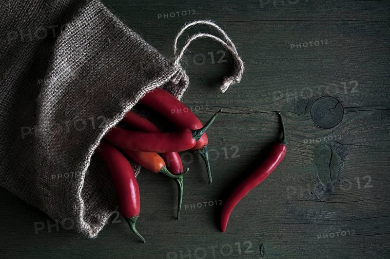 Red peppers in a jute sack lying on a wooden table