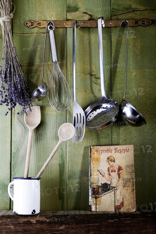 Old cookbook with cooking utensils in front of a green wooden wall