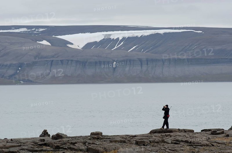 Person with a rifle over their shoulder looking around with binoculars for polar bears