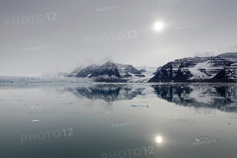 Perfect reflection of mountains and glacial scenery in the pale sunshine of an overcast stormy day
