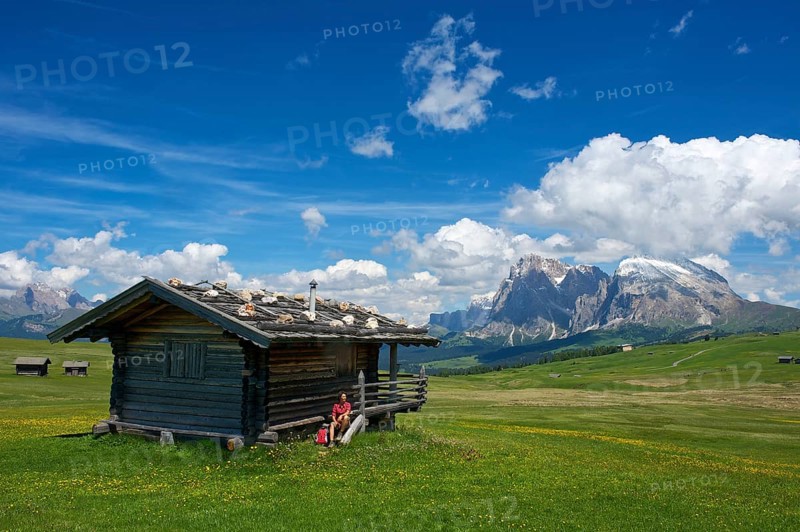 Woman sitting at an alpine hut in front of Piatto Mountain and Sasso Lungo Mountains